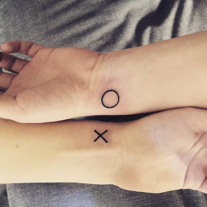 Brother and sister tattoos of an X and O on wrists, symbolizing connection.