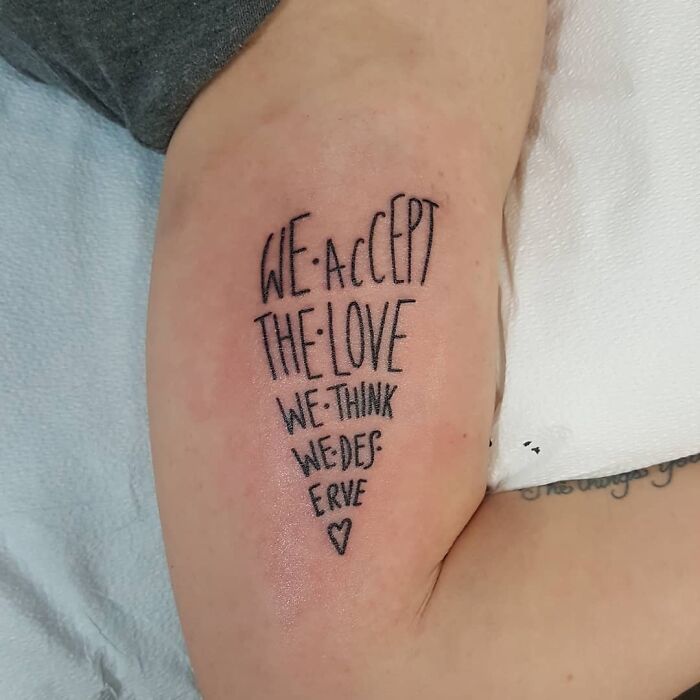 Creative word tattoo on arm: "We accept the love we think we deserve" with a small heart symbol.