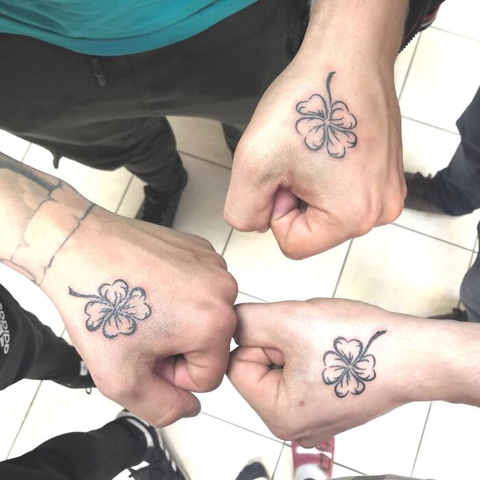 Three hands with matching four-leaf clover brother and sister tattoos, symbolizing unity and connection.