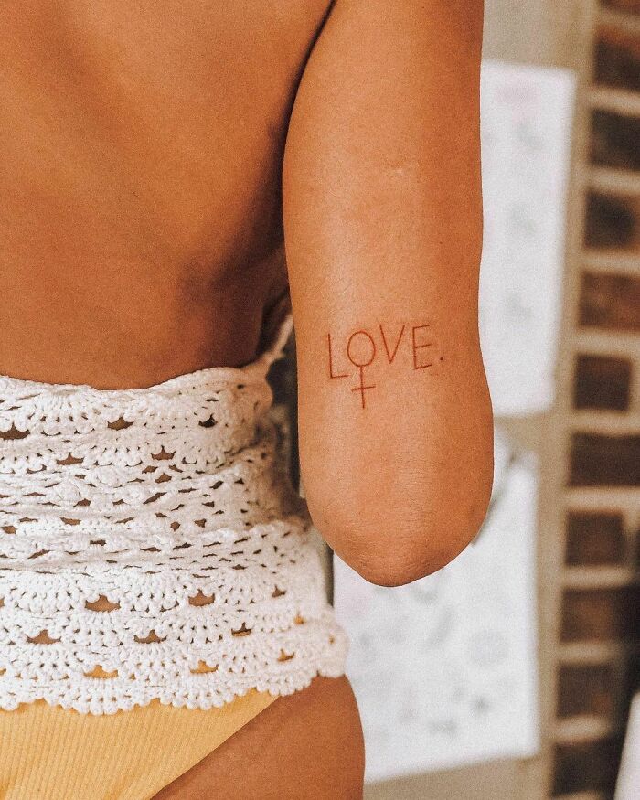 A woman shows a "LOVE" tattoo on her arm, wearing a crochet top, embodying word tattoos' heartful expression.