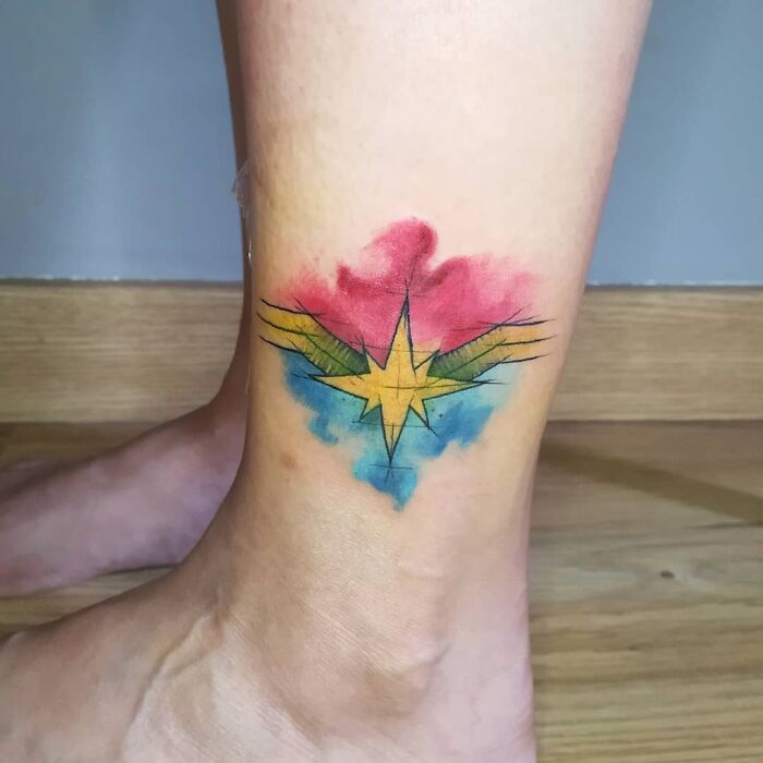 Colorful Marvel tattoo featuring a star and wings design on a person's ankle.