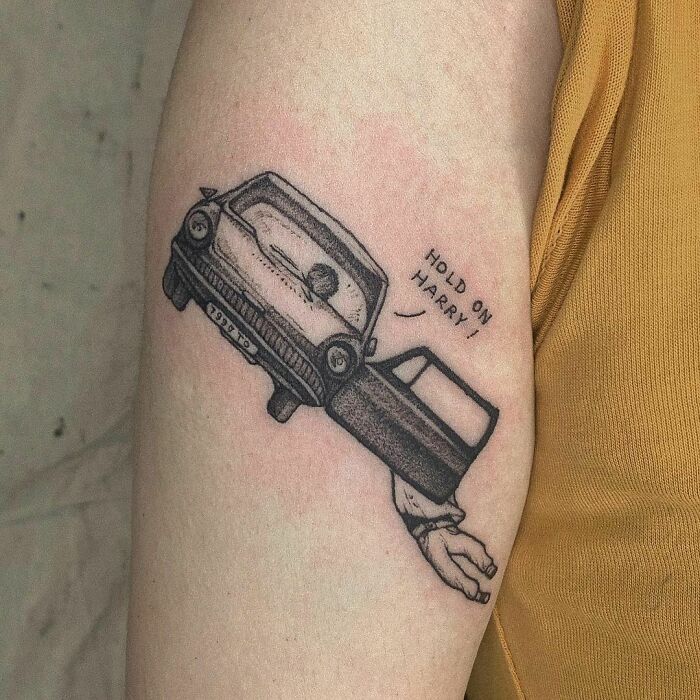 Tattoo of a flying car with "Hold on Harry!" text, inspired by the Wizarding World, on a person's arm.