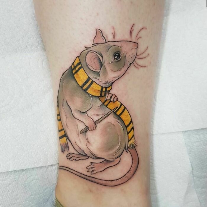 Harry Potter tattoo of a rat with a yellow and black scarf on a person's leg.