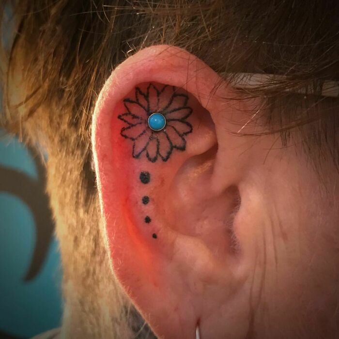 Ear with a flower tattoo and blue stud, showcasing subtle ear tattoo design.