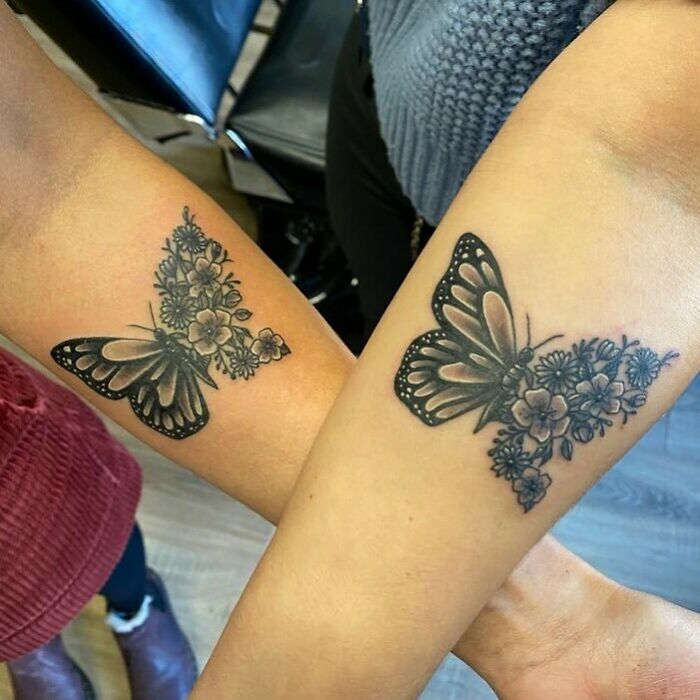 Two arms featuring matching butterfly and floral tattoos, symbolizing sibling connection.