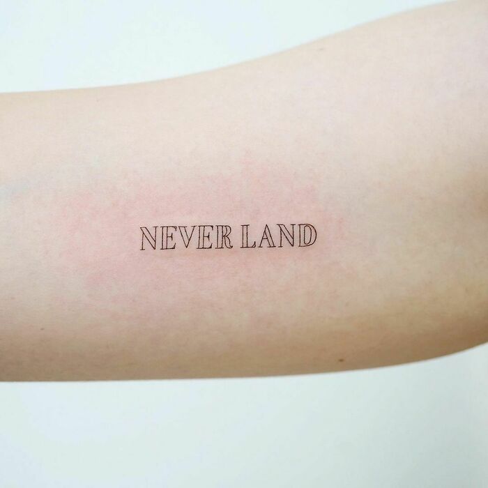 "Minimalist word tattoo 'NEVER LAND' on forearm, perfect for new ink ideas."