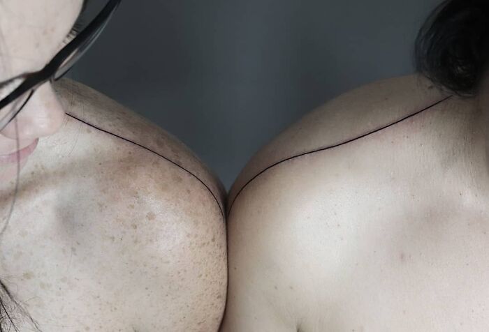 Two shoulders connected by a single-line tattoo, showcasing fine-line perfection.