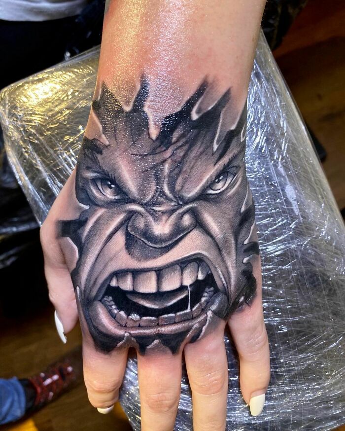 Hand adorned with a detailed Marvel tattoo of a powerful, angry face.