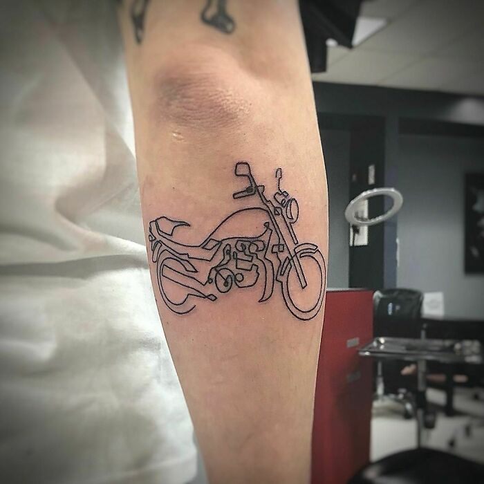 Minimalist line tattoo of a motorcycle on an arm in a tattoo studio.