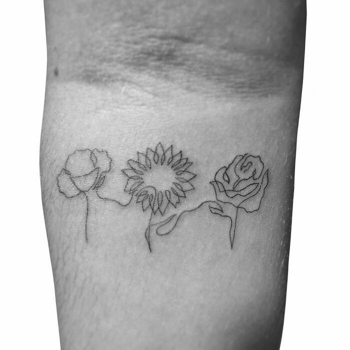 Minimalist line tattoo of three flowers on skin, showcasing unique line art for tattoo enthusiasts.