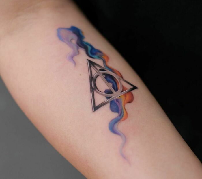 Harry Potter tattoo featuring the Deathly Hallows symbol with colorful abstract design.