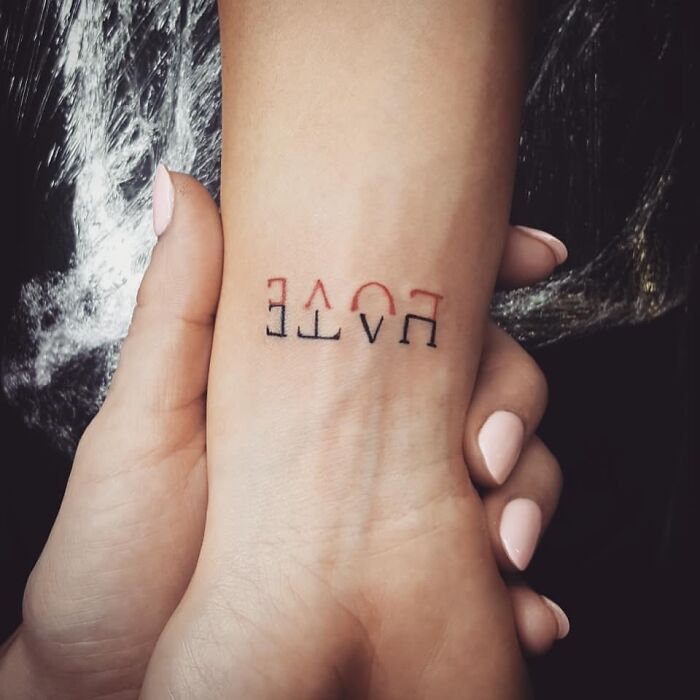 Upside-down "LOVE" tattoo on a wrist, held gently by a hand.