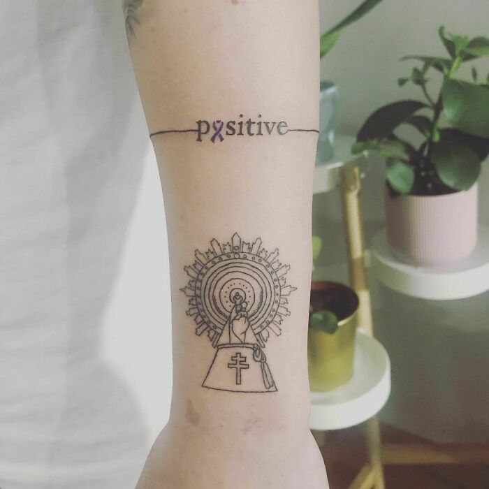 Forearm with a "positive" word tattoo and intricate religious design, showcasing creative word tattoos.