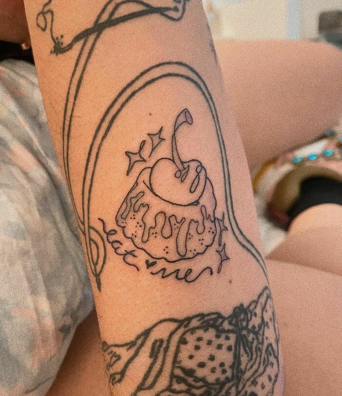 Minimalist tattoo of a melting cake with a cherry and "eat me" text on an arm; unique word tattoo idea.