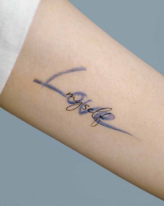 Creative word tattoo on arm with the word "myself" in cursive script and blue accents.