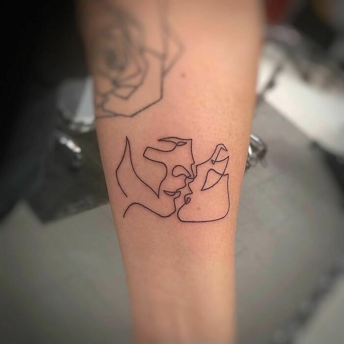 Single-line tattoo of abstract faces kissing on an arm, showcasing minimalist beauty.