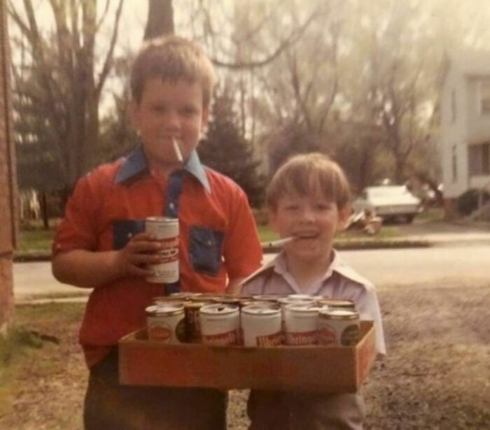 Two small kids holding beer cans in their hands and cigarettes in their mouth 