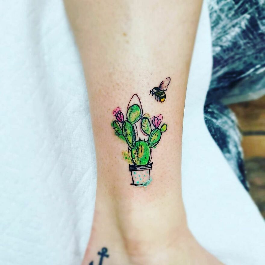 Watercolor tattoo of a cactus with flowers and a bee, inked on a person's arm.
