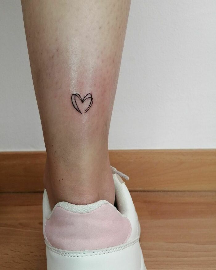 Minimalism line tattoo of a heart on the calf, near white sneakers.