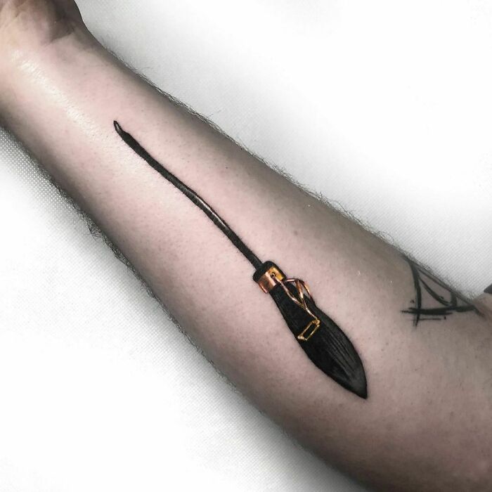 Broomstick tattoo on forearm, inspired by Harry Potter, with minimalist design and fine details.