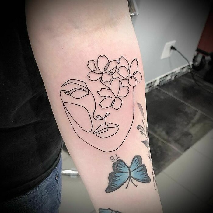 Minimalism tattoo featuring a floral and face line design on an arm.