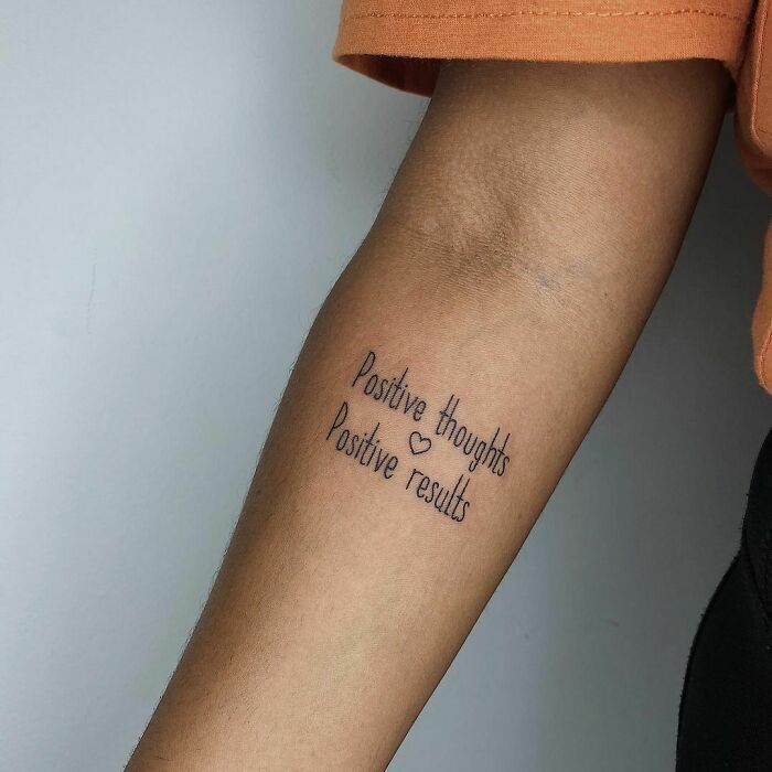 "Word tattoo on forearm reading 'Positive thoughts, Positive results' in black ink."