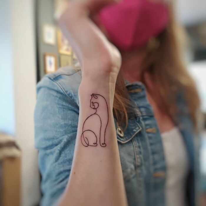 Single-line tattoo of a cat on a person's forearm, showcasing minimalist design in black ink.