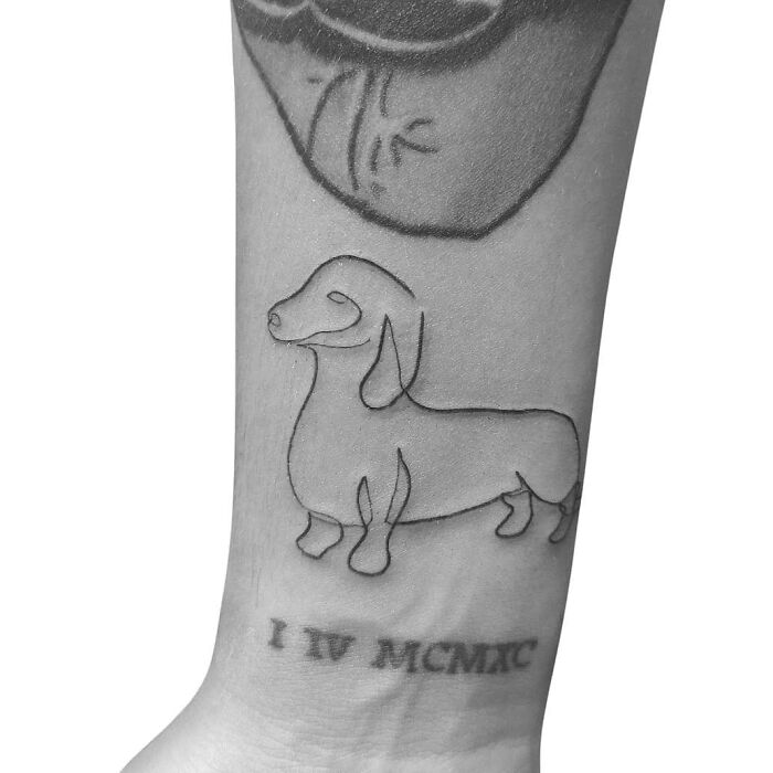 Single-line tattoo of a dachshund on a forearm, capturing its minimalist design and elegance.
