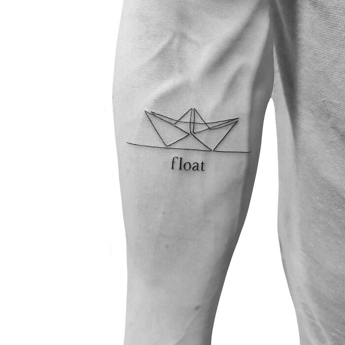 Minimalism line tattoo of a paper boat with the word "float" on an arm.