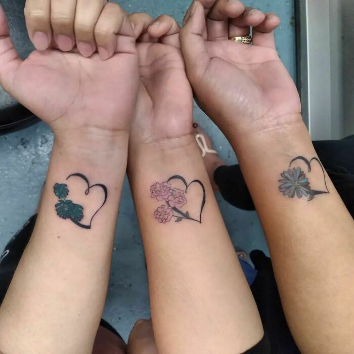 Three wrists with matching heart tattoos featuring flowers, symbolizing friendship.