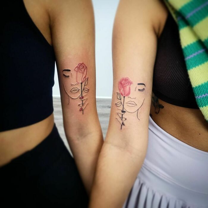 Matching best friend tattoos featuring a minimalist face with a red rose on two people's arms.