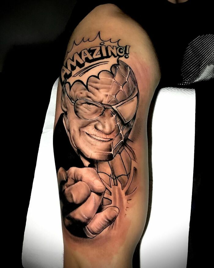 Arm tattoo of a smiling man with "Amazing!" text, blending with a superhero mask design; Marvel tattoo art.