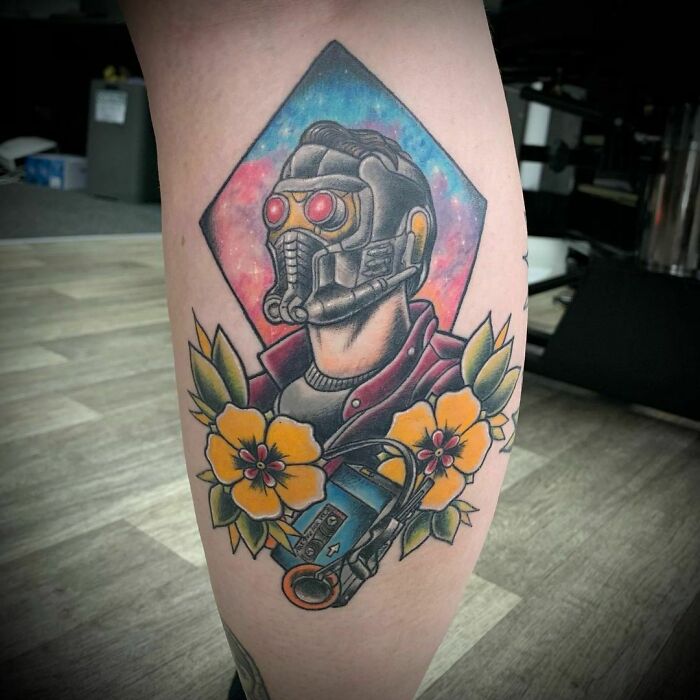 Tattoo of a Marvel character with a helmet, surrounded by vibrant flowers on a person's leg.