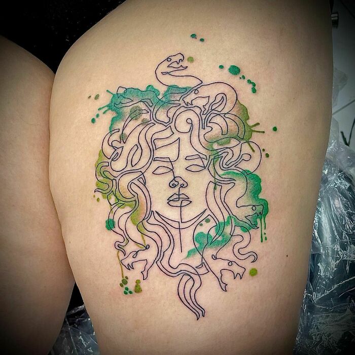 Minimalist line tattoo of Medusa with green accents on the skin.