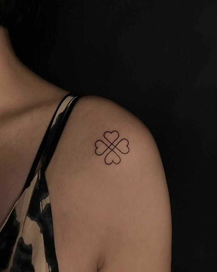 Single-line tattoo of a four-heart design on a person's shoulder, showcasing fine-line perfection.