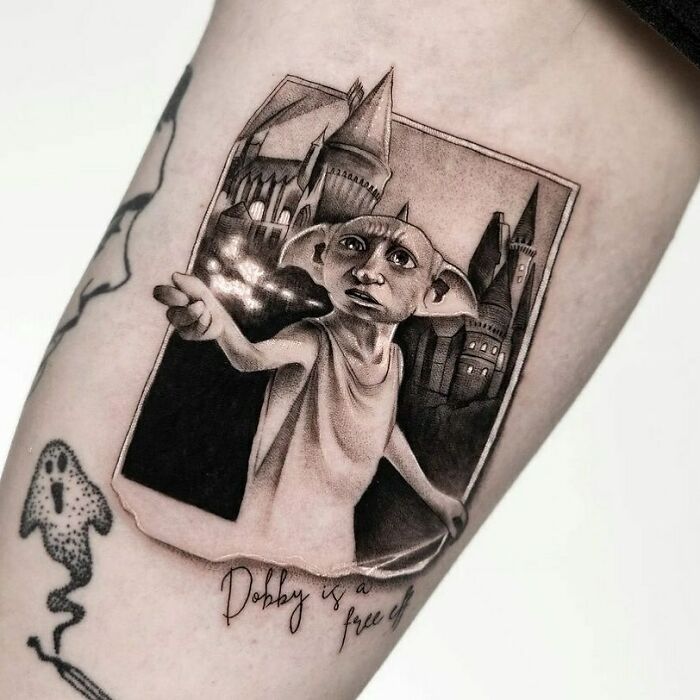 Tattoo of Dobby with Hogwarts in the background, featuring text "Dobby is a free elf" for Harry Potter fans.