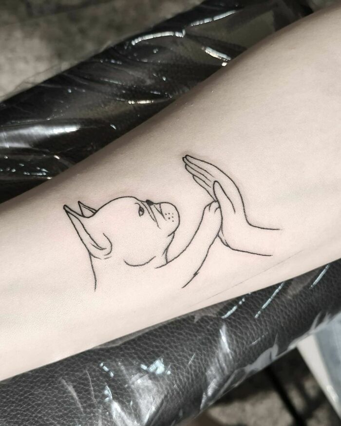 Minimalistic tattoo of a dog high-fiving a hand, symbolizing an adorable pet bond.