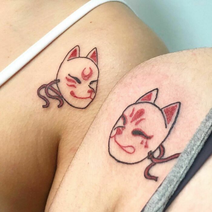 Matching best friend tattoos of fox masks on shoulders, celebrating friendship with unique designs.