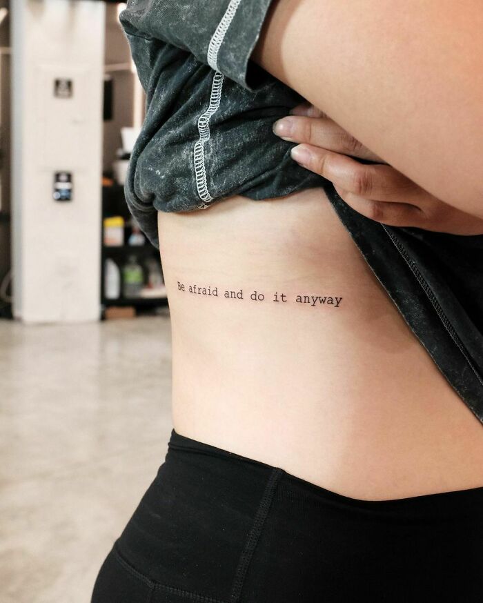 Rib tattoo saying "Be afraid and do it anyway," showcasing creative word tattoos for inkspiration.