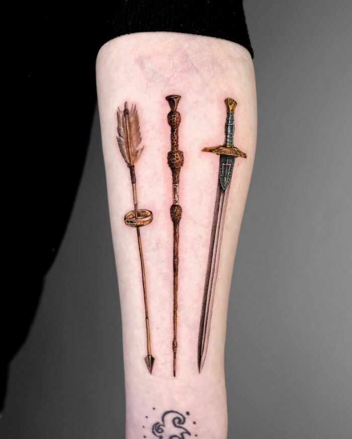 Harry Potter tattoo on arm featuring an arrow, magic wand, and sword design.