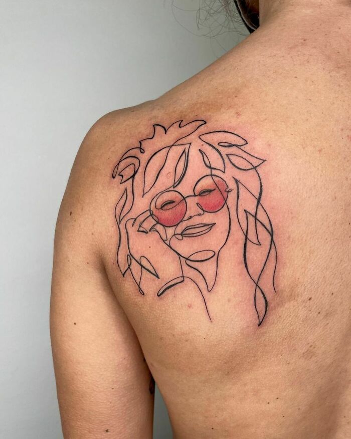 Fine-line tattoo of a face with glasses on a person's back, showcasing single-line artistry.