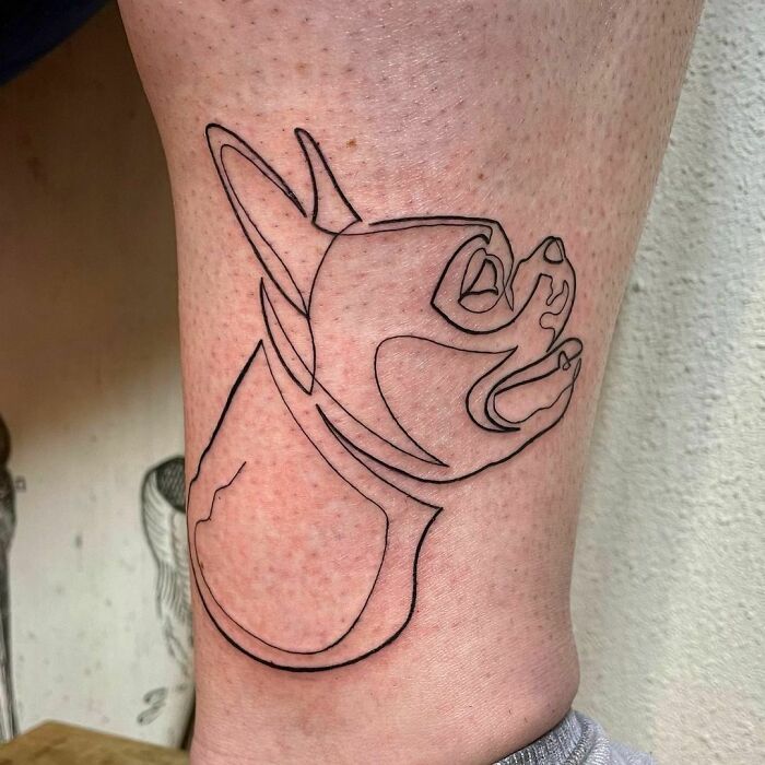 Single-line tattoo of a dog's profile in fine-line style on the leg.