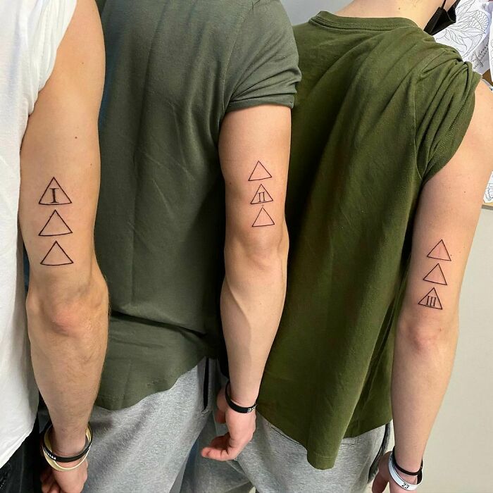 Three siblings showing off simple brother and sister triangle tattoos on their arms, wearing casual clothing.