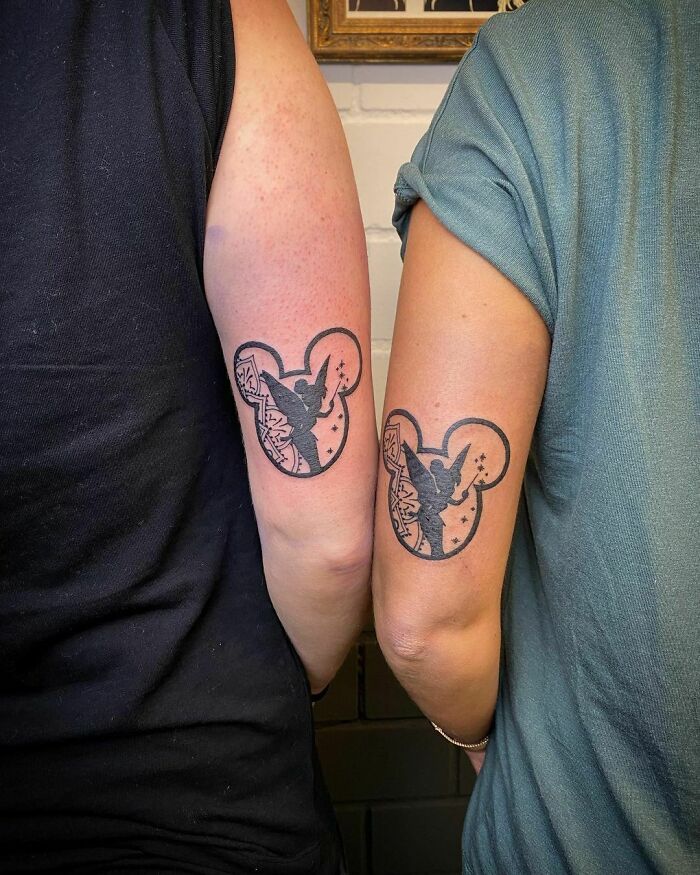 Matching best friend tattoos on arms, featuring silhouette design inside mouse ear shapes, symbolizing friendship.