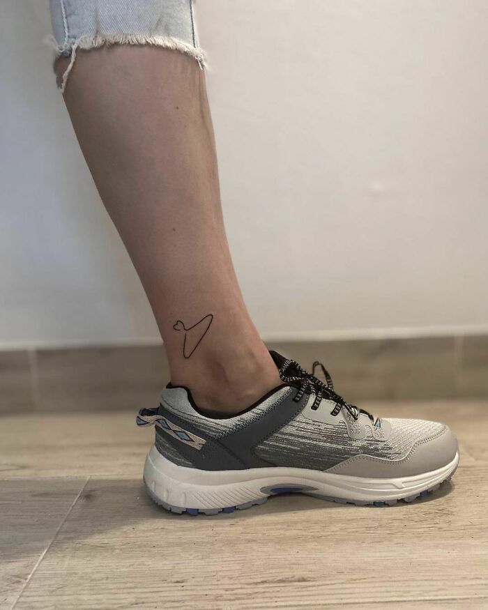 Minimalism line tattoo on ankle above gray sneaker.