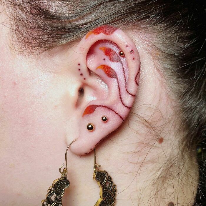 Ear with intricate tattoo design and piercings, showcasing bold ear tattoo ideas.