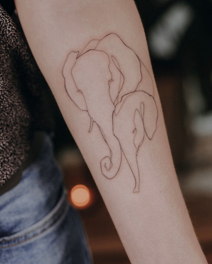 Single-line tattoo of an elephant drawn on a person's forearm.