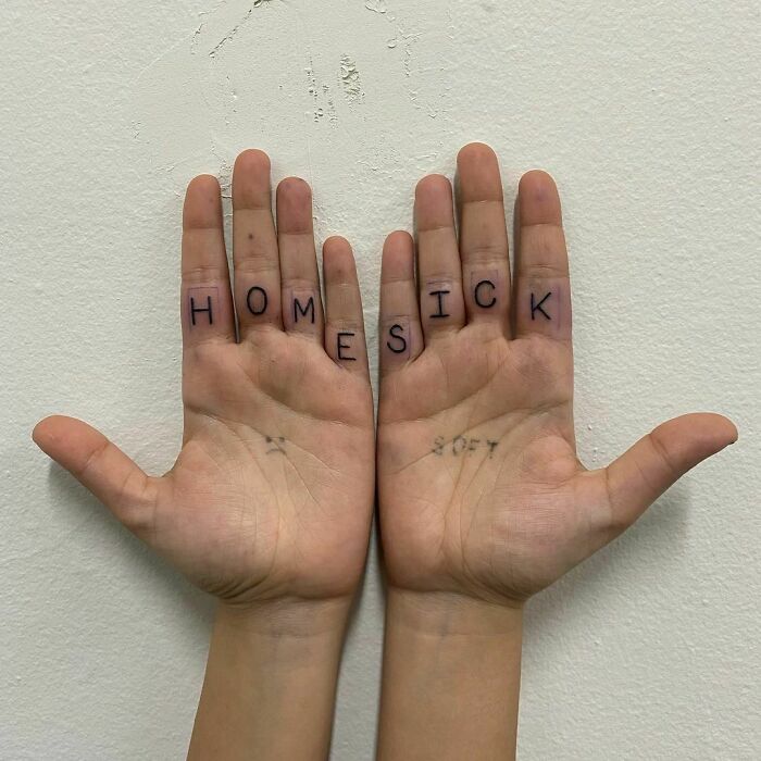 Hands with "HOMESICK" tattooed on fingers, reflecting word tattoo inspiration.
