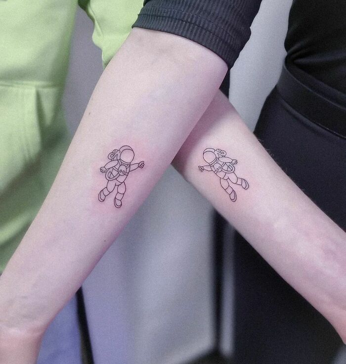 Brother and sister matching astronaut tattoos on forearms, symbolizing unity.