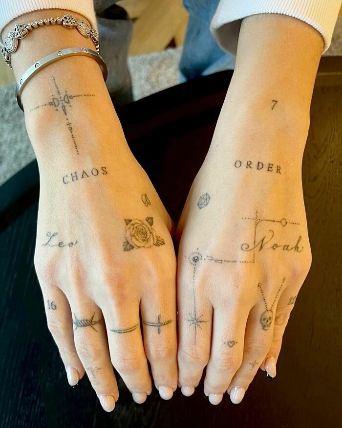 Hands with word tattoos like "Chaos" and "Order," adorned with symbols and small designs, showcasing unique skin art.